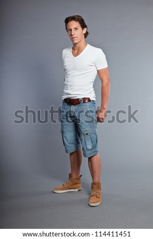 Teenage boy with brown hair and eyes. Wearing white t-shirt and blue shorts. Good looking. Casual wear. Expressions. Studio portrait isolated on grey background.
