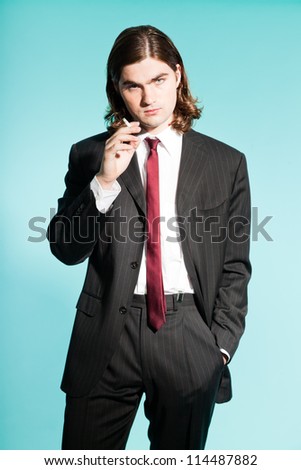 Cool business man with long brown hair confident looking. Smoking cigarette. Wearing black striped suit and dark red tie. Standing out guy. Isolated on light blue background. Studio shot.