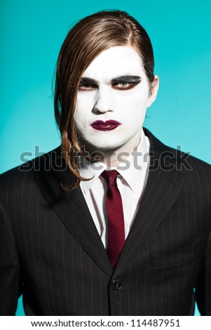 Gothic vampire looking business man wearing black striped suit and dark red tie. Another kind. Scary white face. Isolated on light blue background. Studio shot.
