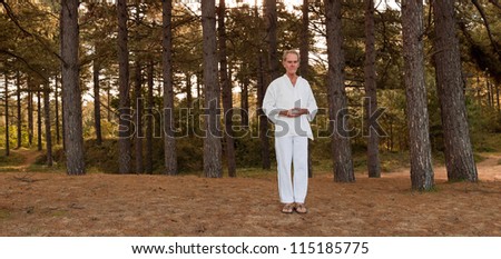 Panoramic shot of meditating senior man in forest. Dressed in white. Peace of mind. Finding balance. Inner rest. Healthy retired living.
