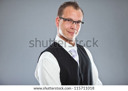 Happy young business man with short hair wearing dark suit with white shirt and purple tie. Wearing glasses. Studio shot isolated on grey background.