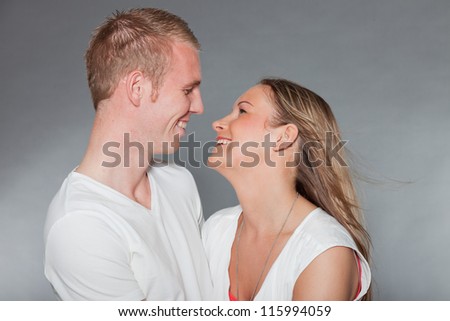 Happy young couple. Kissing. Casual dressed. White shirt. Blue pants. Brown pants. Man short blonde hair. Woman long brown hair. Studio shot isolated on grey background.