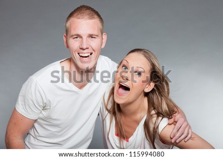 Happy young couple. Casual dressed. White shirt. Blue pants. Brown pants. Man short blonde hair. Woman long brown hair. Studio shot isolated on grey background.