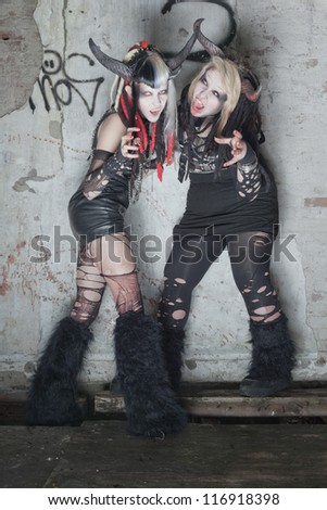 Two scary hungry female demons in front of dirty old wall.