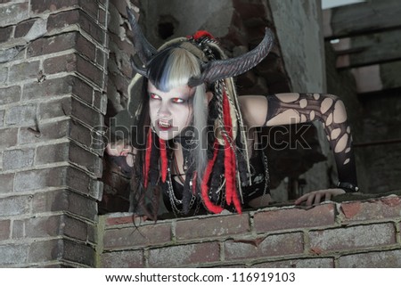Scary hungry female demon crawling over old dirty brick wall.