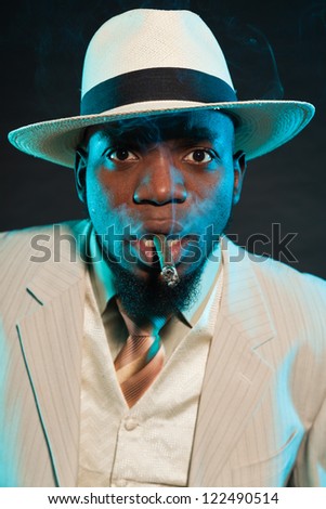 Black american mafia gangster man in suit smoking cigar.