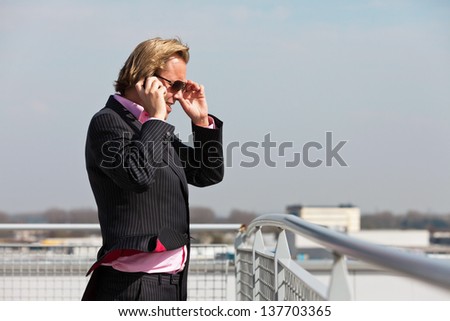 Business man with sunglasses calling with cellphone outdoor on rooftop.