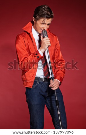 Retro fifties singer wearing red jacket with jeans and tie. Vintage microphone.