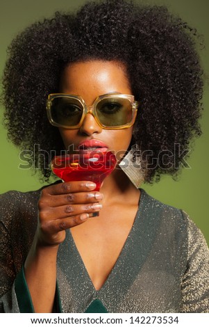 Retro 70s afro fashion woman with green dress and orange cocktail glass. Green background.