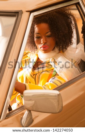 Retro 70s fashion african american woman driving in gold seventies car.