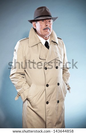 Retro detective man with mustache and hat. Wearing raincoat. Studio shot.