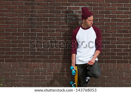 Hip cool urban fashion skateboarder with woolen hat posing in front of brick wall.