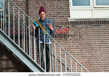 Cool skateboarder with woolen hat standing on iron stairway. His skateboard slides on rail.