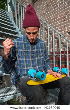 Urban skateboarder with woolen hat checking wheels of his skateboard sitting on iron stairs.