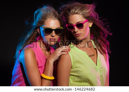 Two sexy retro 80s fashion girls with long blonde hair and sunglasses. Twin sisters together.
