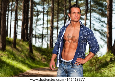 Good looking muscled fitness man with blue lumberjack shirt in forest.