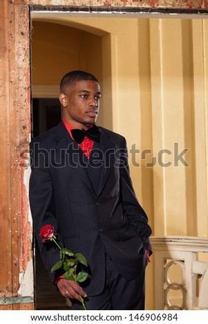 Vintage fashion afro american groom holding red rose. Standing in doorpost of an old house.