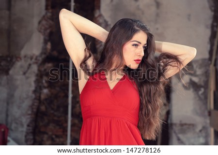 Sensual fashion woman wearing red dress posing in old urban building. Long hair. Brunette.