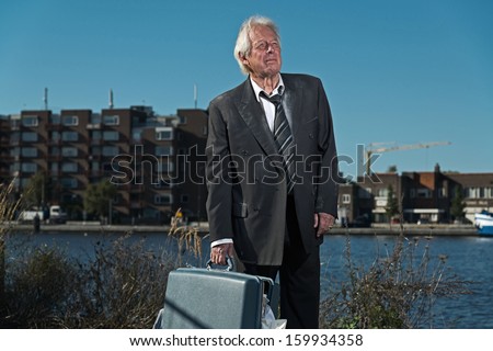 Senior business man without a job and homeless on the street. Holding a suitcase. Dirty suit.