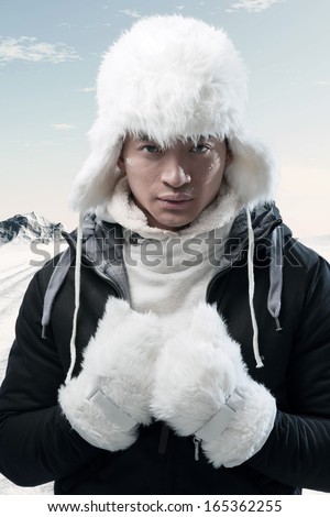 Asian winter fashion man in snow mountain landscape. Wearing black jacket with white furry hat and gloves.