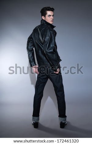 Retro rock and roll 50s fashion man with dark grease hair. Wearing black leather jacket and jeans. Studio shot against grey.