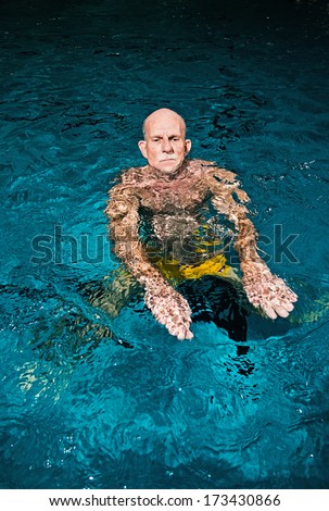 Healthy active senior man with beard in indoor swimming pool. Wearing yellow swimming trunks.