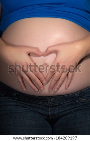 Pregnancy belly with hands of mom creating a heart shape. Close-up.
