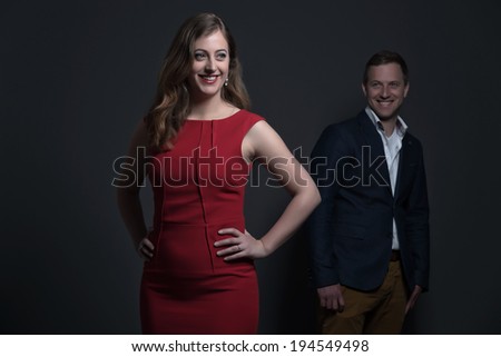 Fashion couple wearing a red dress and blue jacket. Young man and woman. Studio shot against grey.