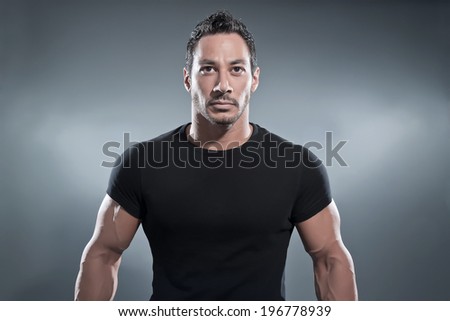 Combat muscled fitness man wearing black shirt and pants. Studio shot against grey.