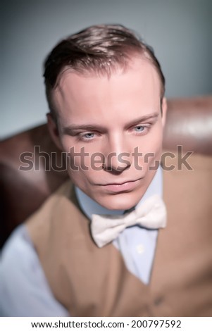 Retro 1920s classic business fashion man sitting in leather chair. Wearing shirt with gilet and bow tie. Studio shot.