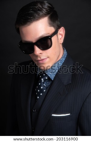 Stylish young business man wearing black retro sunglasses and dark blue jacket with tie. Studio shot against black.