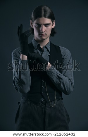 Mysterious western 1900 fashion man with brown hair wearing gloves. Studio shot against grey.