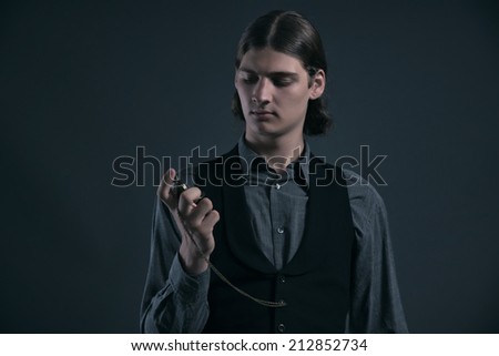 Western 1900 fashion man with brown hair looking at watch. Studio shot against grey.