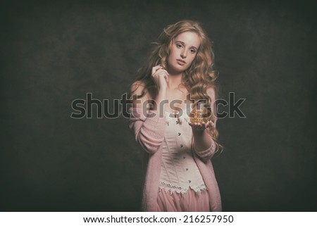 Vintage fashion woman holding old perfume bottle. Wearing pink corset with dress. Studio shot.