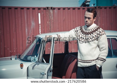 Retro fifties fashion man with woolen sweater standing against vintage car.