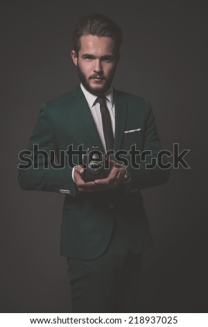 Business fashion man wearing green suit with white shirt and black tie. Holding vintage camera. Studio shot against grey.