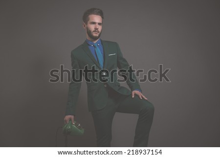 Business fashion man wearing green suit with blue shirt and tie. Holding vintage telephone. Studio shot against grey.