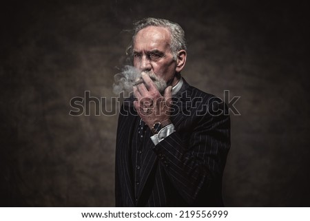 Cigar smoking characteristic senior business man with gray hair and beard wearing blue striped suit and tie. Against brown wall.