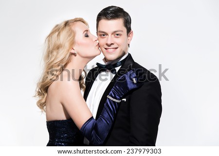 Romantic new year\'s eve fashion couple. Woman kissing man. Wearing black dinner jacket and blue dress. Isolated against white.