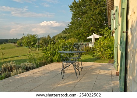 Paved outdoor patio with a green wrought iron table and chairs overlooking lush countryside with umbrellas visible behind