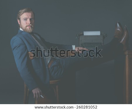Successful vintage businessman relaxing in the office with his feet on the desk alongside an old manual typewriter looking thoughtfully to the side with a pensive expression