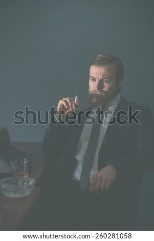 Vintage businessman sitting in his office at his desk smoking a cigarette and staring thoughtfully at the floor