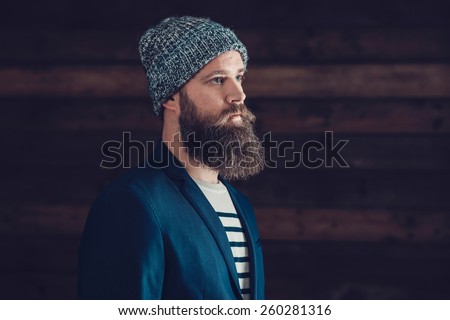 Close up Side View of a Serious Goatee Man with Gray Bonnet Looking to the Right of the Frame with Wooden Wall Background.