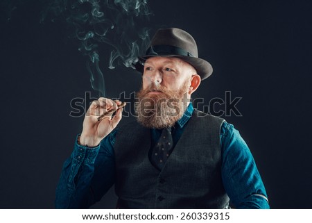 Close up Middle Age Man with Long Goatee, Wearing Formal Wear with Cap, Smoking a Cigarette While Looking at the Far left of the Frame. Isolated on a Background.