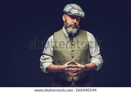 Half Body Shot of a Middle Age Man in a Trendy Green Outfit with Ivy Cap, Posing on Black Background with Hands In front his Belly While Looking at the Camera Seriously.