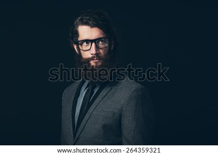 Close up Gorgeous Young Man with Long Goatee Beard, Wearing Formal Fashion with Eyeglasses, Looking to the Upper Right of the Frame on a Black Background.