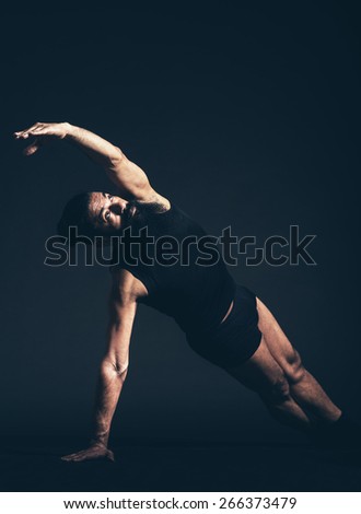 Serious Athletic Man with Long Goatee Beard Doing a Floor Exercise, Performing Side Plank, A Powerful Arm and Wrist Strengthener Pose. Captured in Studio on Black Background