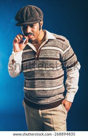 Sexy Afro-American man standing with his hand in his pocket wearing a retro cloth cap enjoying a cigarette
