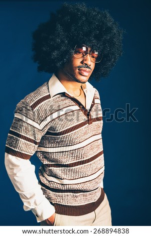 Close up Portrait of a Stylish Afro-American Man with Long Curly Hairstyle, Posing in Trendy Shirt and Glasses Fashion with Hands in the Pocket. Isolated on Dark Blue Background.