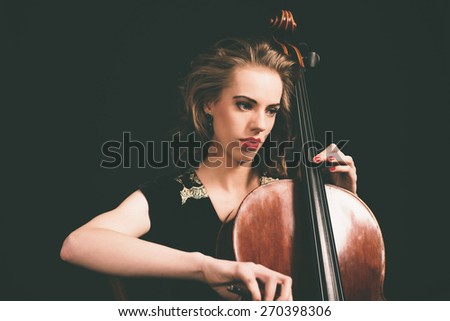 Pretty young female musician playing the cello at a classical recital concentrating on her notes in the darkness, close up view